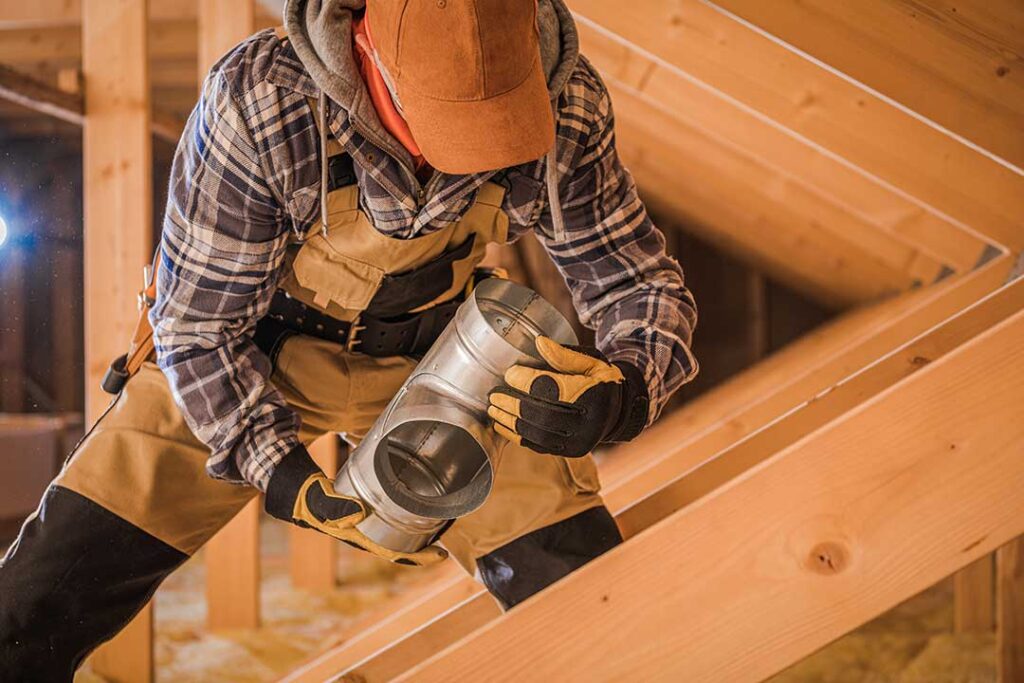A worker using a vacuum hose to clean ceiling air ducts in a residential living room.